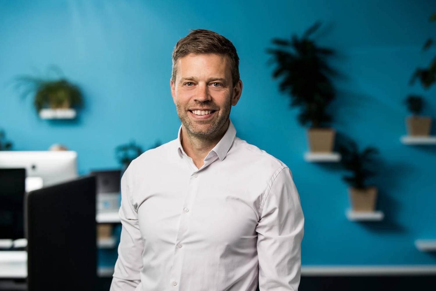 Tor Magnus, grunnlegger av markedsføringsselskapet Inbound, smiler foran en moderne kontorvegg med blå bakgrunn og grønne planter.