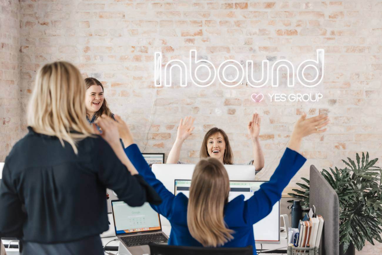 Glade kollegaer som feirer på et moderne kontor med ‘Inbound’ neon-skilt i bakgrunnen.