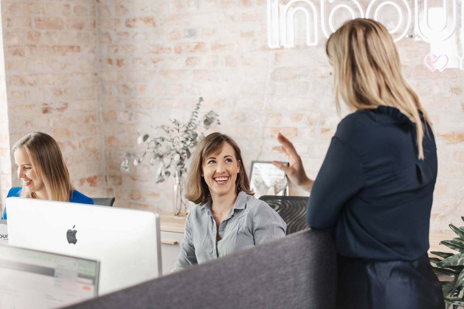 Kollegaer i en samtale på et moderne kontor med ‘Inbound’ neon-skilt i bakgrunnen
